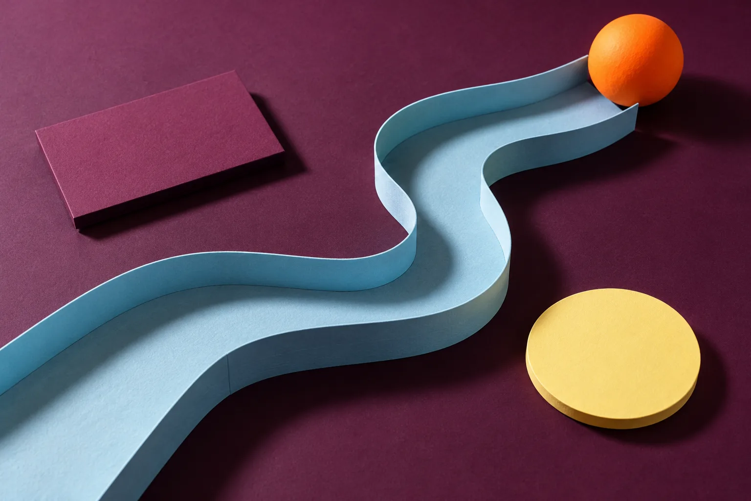A curved blue paper track linking a bright orange sphere with distinct colored shapes