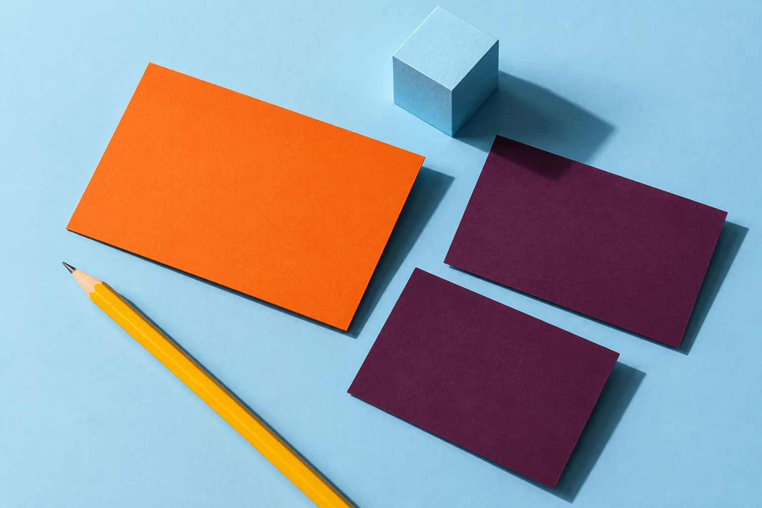 Blank creative cards, a yellow pencil, and a blue paper cube arranged as a study in experimentation