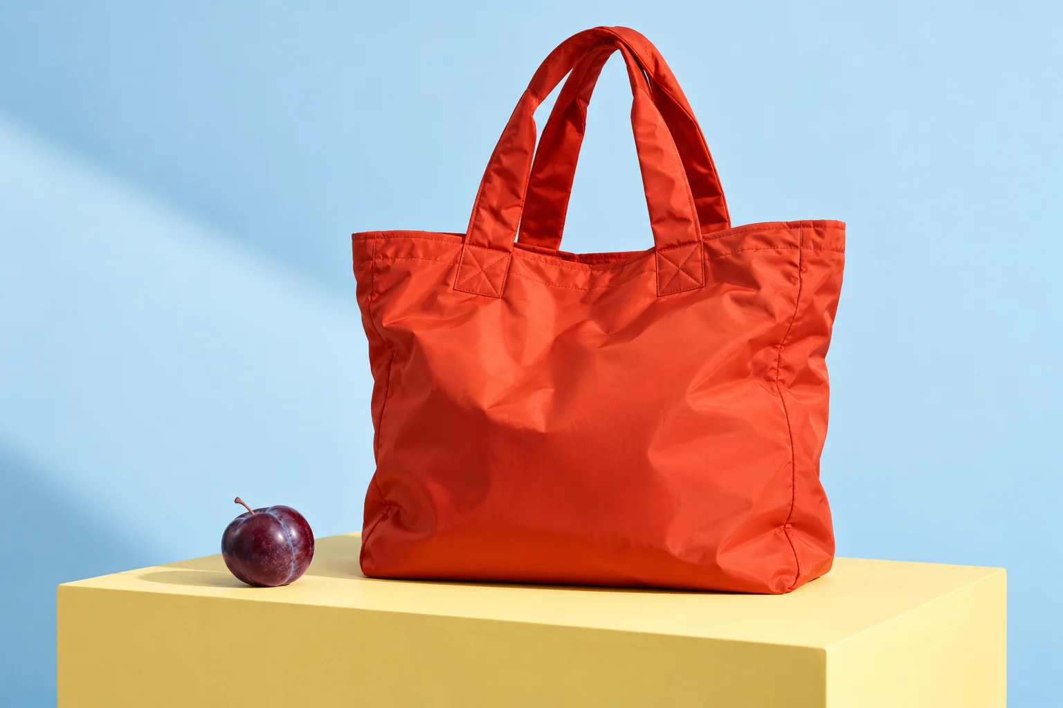 An orange tote bag on a yellow plinth against a glacier-blue backdrop